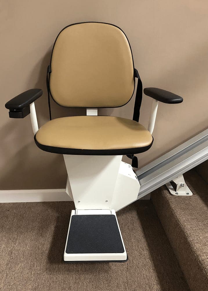 Stair chair with a tan padded seat and armrests at the foot of a staircase